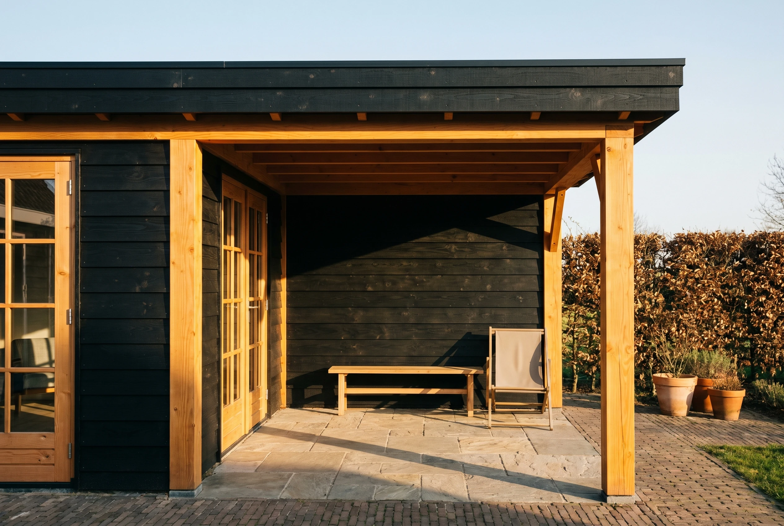 De overkapping van het tuinhuis met douglashouten stijlen boven een bestraat terras met bank en stoel