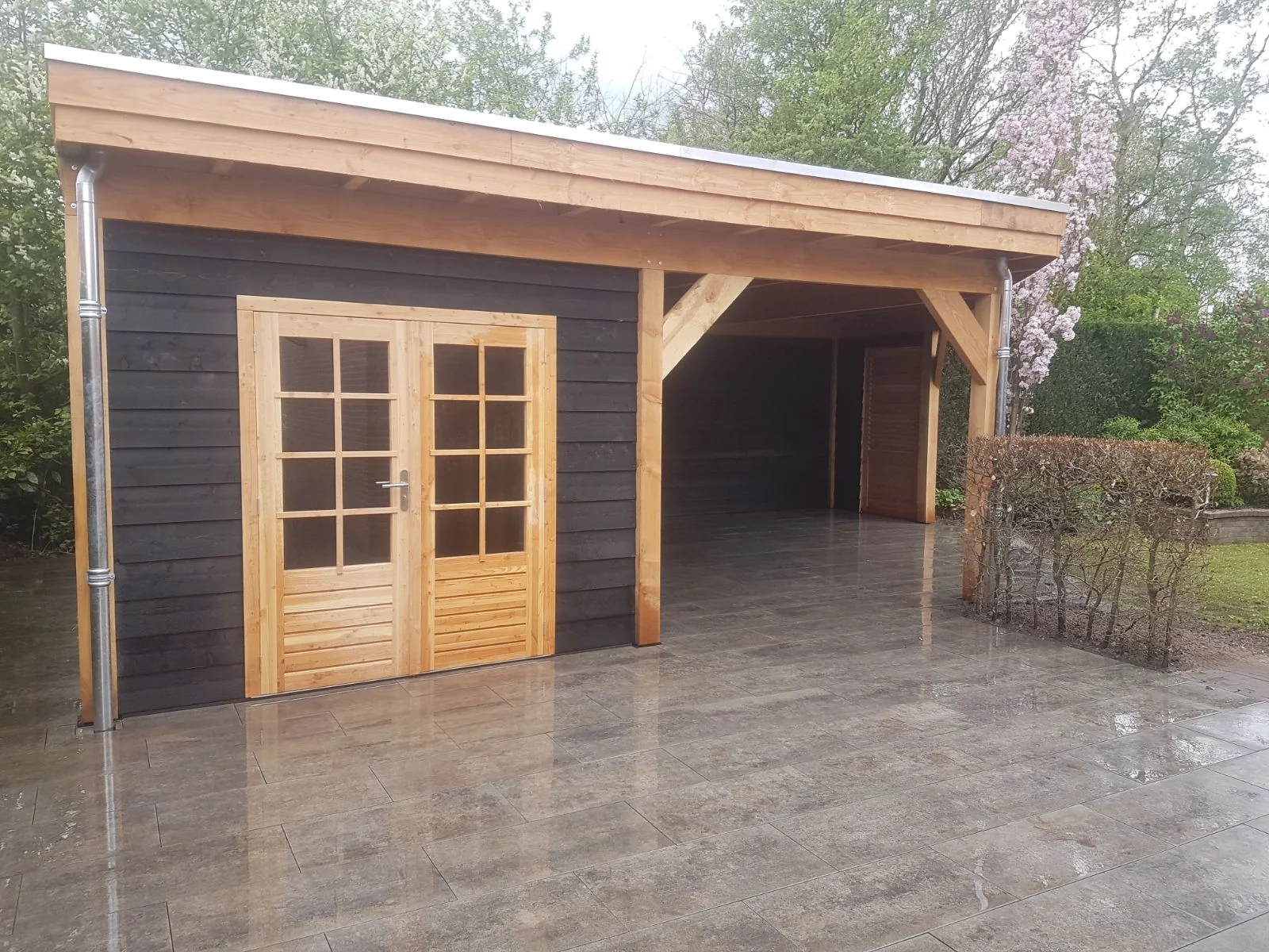 Zwart tuinhuis met douglashouten frame, openslaande deuren met roeden en een aangebouwde overkapping