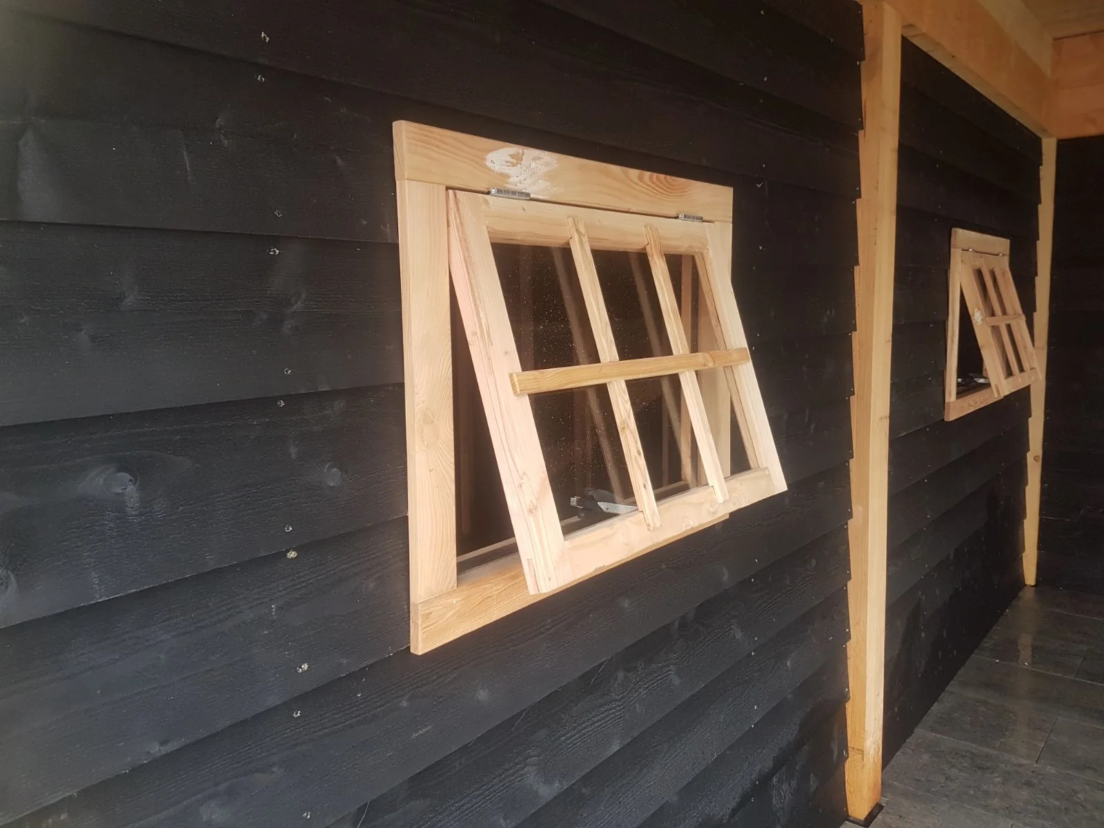 Detail van de openslaande houten raampjes met roeden in de zwarte gevel